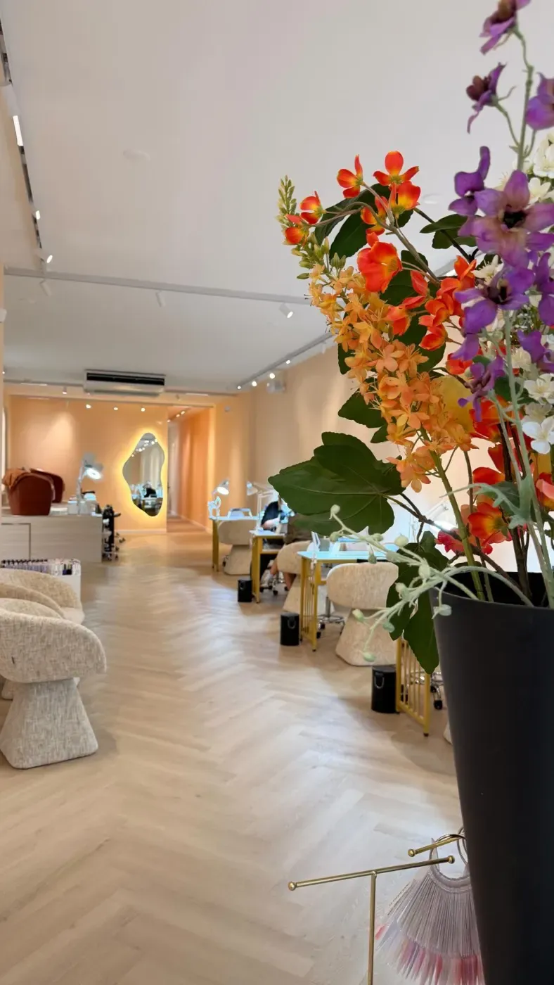 De entree van Bellamy Beauty Bar: bloemen, bouclé stoelen en de gloeiende ovale spiegel achterin de salon