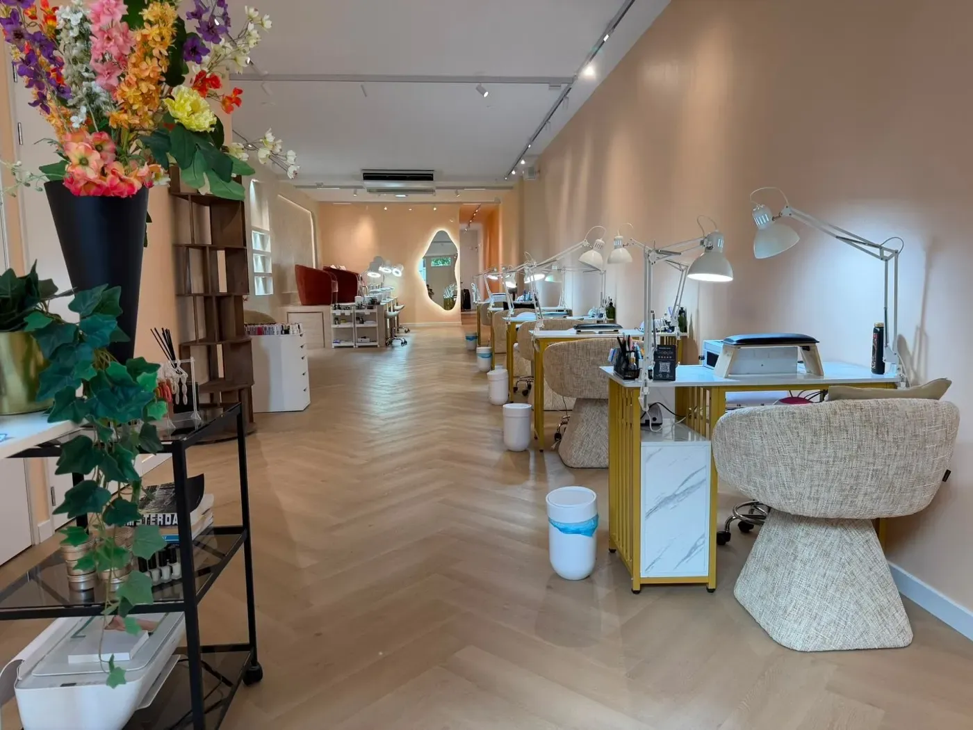 De lange salon van Bellamy Beauty Bar: perzikkleurige muren, visgraatvloer, de gloeiende ovale spiegel en gouden manicuretafels