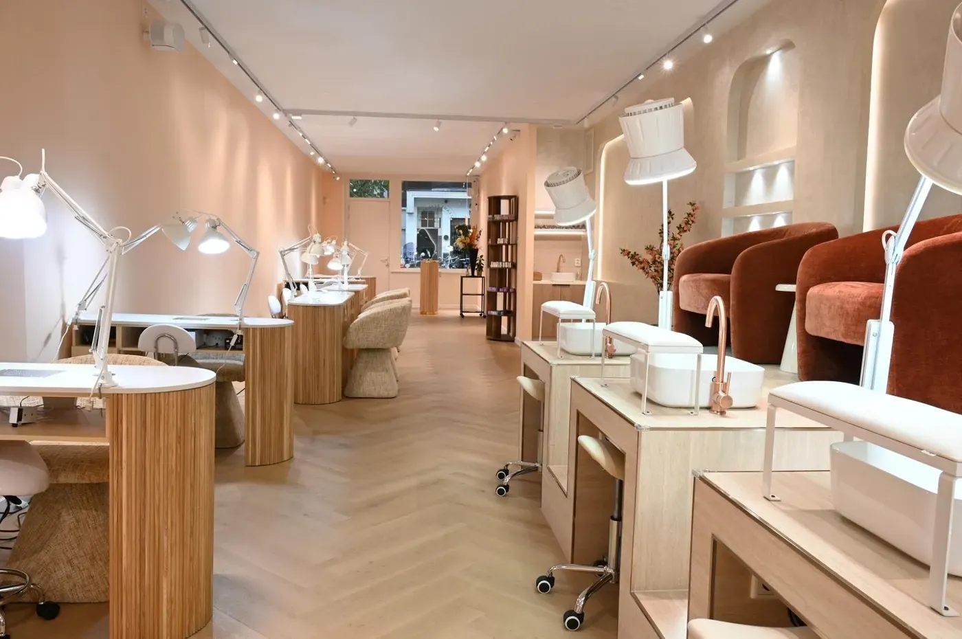De salon met manicuretafels, pedicureplekken en roestkleurige fluwelen stoelen